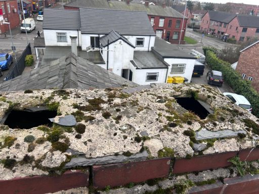 Weathered rooftop with holes, showing moss and surrounding residential buildings.